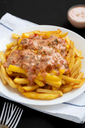 Homemade Animal Style French Fries on a white plate on a black background, low angle view.