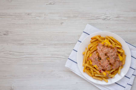 Homemade Animal Style French Fries on a white plate on a white wooden background, overhead view....