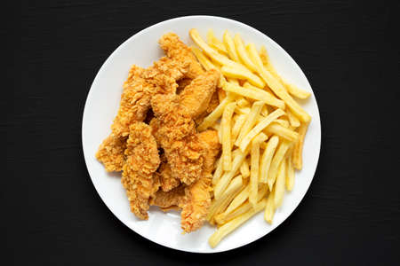 Homemade Crispy Chicken Tenders and French Fries on a white plate on a black background, top view. Flat lay, overhead, from above.の写真素材