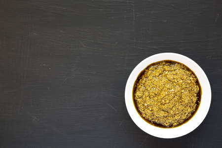 Homemade Basil Pesto with Parmesan and Pine Nuts on a black surface, top view. Flat lay, overhead,...