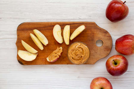 Raw Red Apples and Peanut Butter on a rustic wooden board on a white wooden surface, top view. Flat lay, overhead, from above.の写真素材