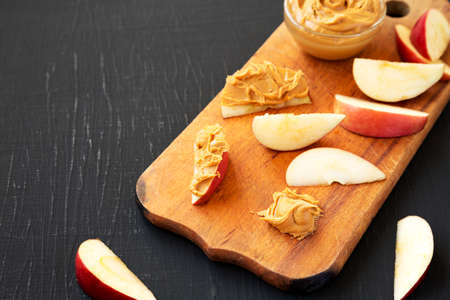 Raw Red Apples and Peanut Butter on a rustic wooden board on a black background, low angle view. Copy space.の写真素材