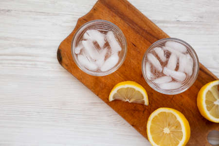 Fresh Lemon Sparkling Water with Ice on a rustic wooden board on a white wooden background, top view. Copy space.の写真素材