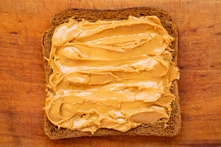 Piece of Bread with Peanut Butter on a rustic wooden board, top view. Close-up.の写真素材