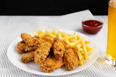 Homemade Crispy Chicken Wings and French Fries on a white plate, glass of cold beer, side view....