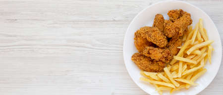 Homemade Crispy Chicken Wings and French Fries on a white plate on a white wooden background, overhead view. From above, top view, flat lay. Copy space.の写真素材