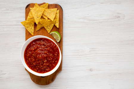 Homemade Tomato Salsa and Nachos on a rustic wooden board on a white wooden background, top view. Flat lay, overhead, from above. Space for text.の写真素材