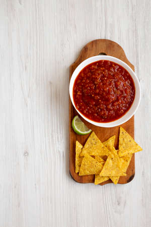 Homemade Tomato Salsa and Nachos on a rustic wooden board on a white wooden background, top view. Flat lay, overhead, from above. Copy space.の写真素材