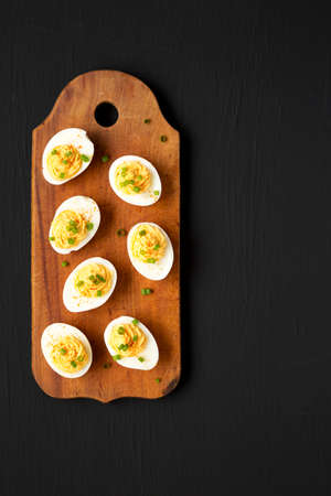Homemade Deviled Eggs with Chives on a rustic wooden board on a black surface, top view. Flat lay, overhead, from above.の写真素材