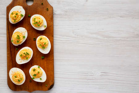 Homemade Deviled Eggs with Chives on a rustic wooden board on a white wooden surface, top view. Flat lay, overhead, from above. Copy space.の写真素材