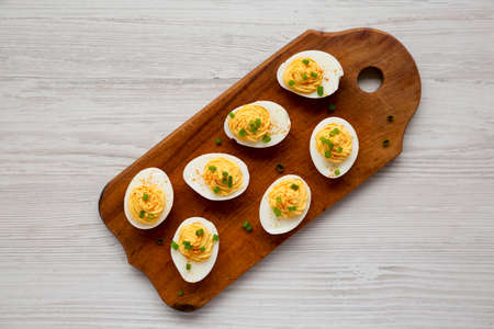 Homemade Deviled Eggs with Chives on a rustic wooden board on a white wooden table, top view. Flat lay, overhead, from above.の写真素材