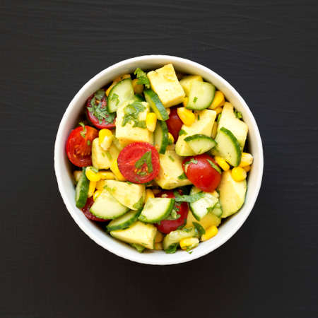 Fresh Avocado Tomato Salad in a bowl on a black background, top view. Flat lay, overhead, from above.の写真素材
