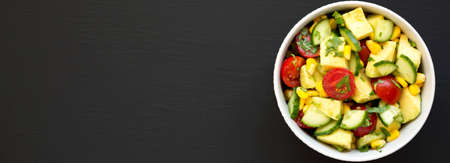 Fresh Avocado Tomato Salad in a bowl on a black surface, top view. Flat lay, overhead, from above. Copy space.の写真素材