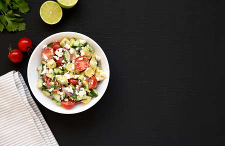 Delicious Avocado Tomato and Cucumber Salad in a white bowl on a black background, top view. Flat lay, overhead. Copy space.の写真素材