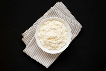 Tasty Ricotta Cheese in a white bowl on a black surface, top view. Overhead, from above, flat lay.の写真素材