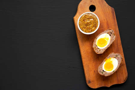 Homemade Scotch Eggs on a rustic wooden board on a black background, top view. Flat lay, overhead, from above. Copy space.の写真素材