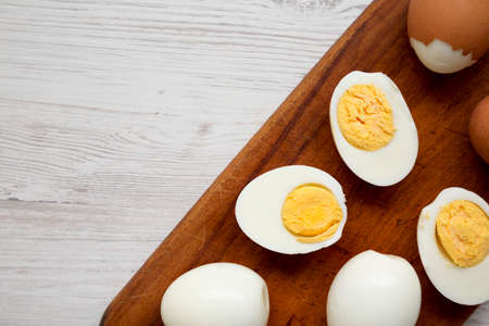 Hard Boiled Eggs on a rustic wooden board on a white wooden background, top view. Copy space.