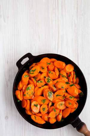 Homemade Sauteed Carrots in a cast iron pan on a white wooden background, overhead view. Flat lay,...