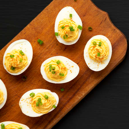 Homemade Deviled Eggs with Chives on a rustic wooden board on a black background, top view. Flat lay, overhead, from above.の写真素材