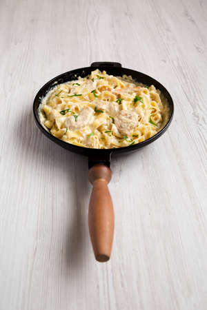 Homemade Chicken Fettuccine Alfredo in a cast-iron pan on a white wooden background, low angle view.の写真素材
