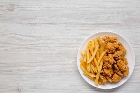 Homemade Fried Chicken Bites and French Fries on a plate on a white wooden surface, overhead view. Flat lay, top view, from above. Copy space.の写真素材
