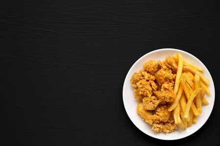 Homemade Fried Chicken Bites and French Fries on a plate on a black background, overhead view. Flat lay, top view, from above. Space for text.の写真素材