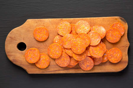 Italian Pepperoni Slices on a rustic wooden board on a black surface, top view. Flat lay, overhead, from above.の写真素材