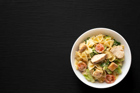 Homemade Chicken Caesar Pasta Salad in a white bowl on a black background, top view. Flat lay, overhead, from above.の写真素材