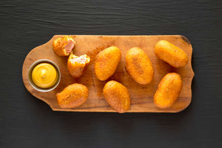 Homemade Mini Corn Dogs on a rustic wooden board on a black surface, top view. Flat lay, overhead, from above.の写真素材