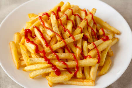 Homemade French Fries with Ketchup, Salt and Pepper on a white plate on a white wooden background,...