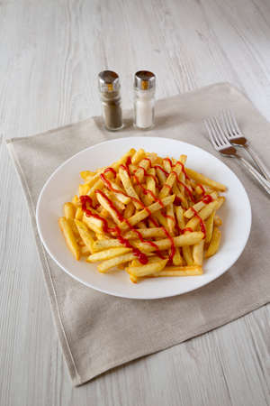 Homemade French Fries with Ketchup, Salt and Pepper on a white plate on a white wooden background, side view.の写真素材