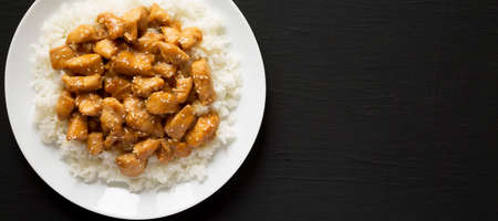 Homemade Orange Chicken with White Rice on a white plate on a black surface, top view. Overhead, from above, flat lay. Copy space.の写真素材