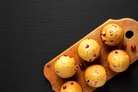 Homemade Cranberry Muffins with Orange Zest on a rustic wooden board on a black background, top...