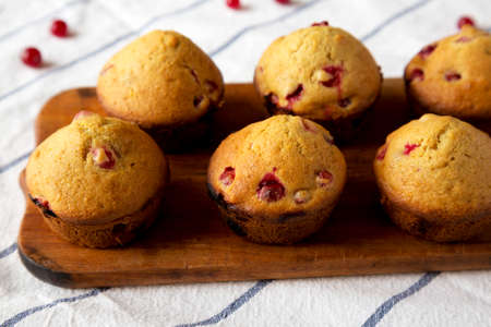 Homemade Cranberry Muffins with Orange Zest on a rustic wooden board on cloth, side view. Close-up.