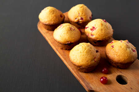Homemade Cranberry Muffins with Orange Zest on a rustic wooden board on a black surface, side view....