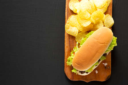 Homemade Chopped Beef Sandwich with Potato Chips on a rustic wooden board on a black background, top...