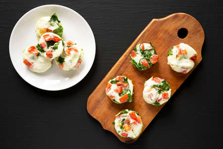 Homemade Egg White Breakfast Cups with Spinach and Tomato on a black background, top view. Flat lay,...