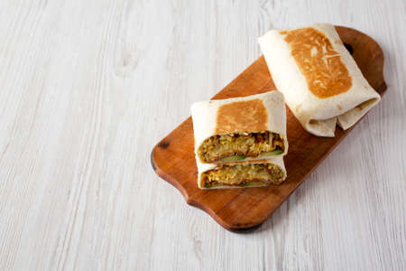Homemade Breakfast Egg Burrito with Avocado and Bacon on a rustic wooden board on a white wooden...