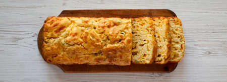 Homemade Cheesy Bread Loaf on a rustic wooden board on a white wooden background, top view.