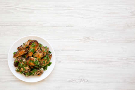 Homemade baked Garlic Parmesan Chicken Wings on a white plate on a white wooden background, top view. Flat lay, overhead, from above. Copy space.の写真素材