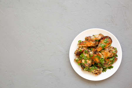 Homemade baked Garlic Parmesan Chicken Wings on a white plate on a gray background, top view. Flat...