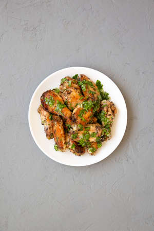 Homemade baked Garlic Parmesan Chicken Wings on a white plate on a gray background, top view. Flat...