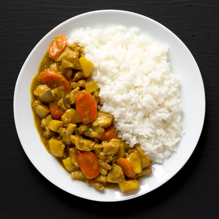Homemade Japanese Chicken Curry on a white plate on a black background, top view. Flat lay, overhead, from above.の写真素材
