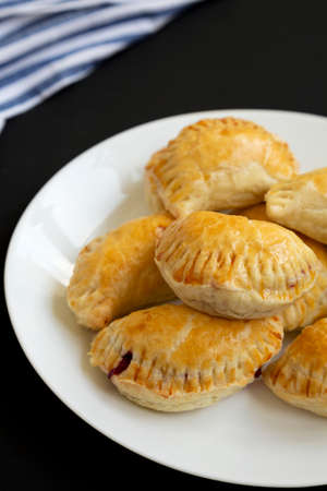 Homemade Cherry Hand Pies on a plate on a black background, side view.