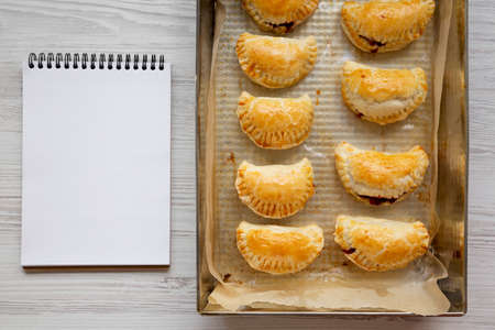 Homemade Cherry Hand Pies in a baking pan, blank notepad, top view. Flat lay, overhead, from above.