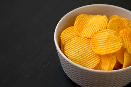 Ruffled Cheese Potato Chips in a Bowl on a black surface, side view. Space for text.