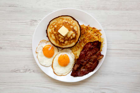 Full American Breakfast with Bacon, Hash Browns, Eggs and Pancakes on a plate on a white wooden background, top view.の写真素材