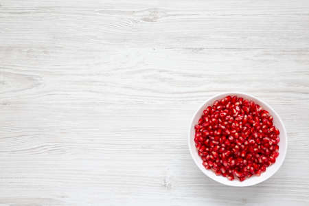 Red Pomegranate Seeds in a Bowl on a white wooden background, top view. Flat lay, overhead, from...