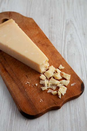 A Piece of Parmigiano Reggiano on a rustic wooden board on a white wooden background, side view.