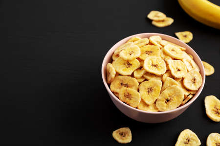 Homemade Banana Chips in a Pink Bowl on a black background, low angle view.の写真素材